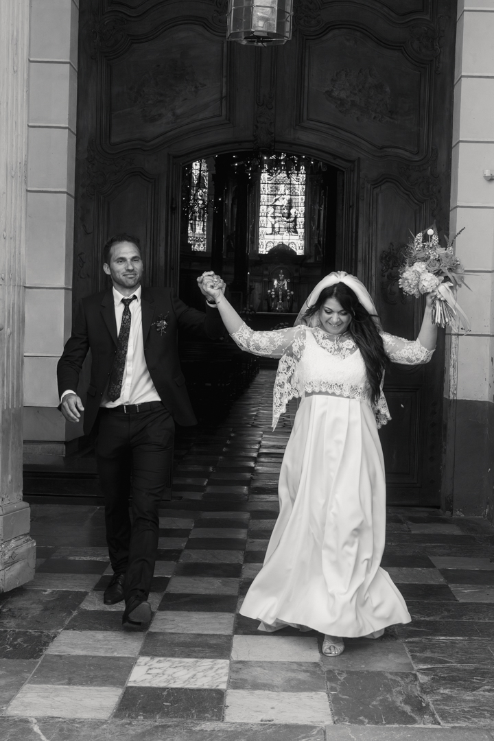 Sortie de mariage éditoriale à la cathédrale de Tarbes : les mariés célèbrent les mains levées en noir et blanc.